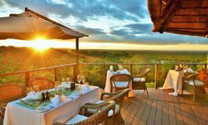 a restaurant with tables and chairs on a deck with the sunset at Victoria Falls Safari Club in Victoria Falls