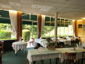 un restaurant avec des tables et des chaises blanches et de grandes fenêtres dans l'établissement Logis Terrasse Hôtel, à Lisieux