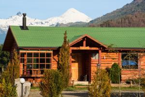 Cabaña de madera con techo verde y montaña en Complejo Turístico Rañintu Epupillan, en Pucón