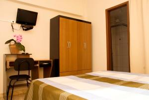 a bedroom with a bed and a cabinet and a desk at Orquídea Hotel in Viçosa