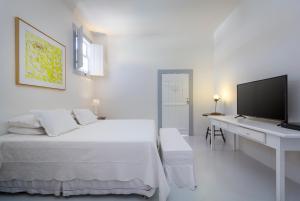 a white bedroom with a bed and a desk with a television at Pousada Casa de Paraty in Paraty