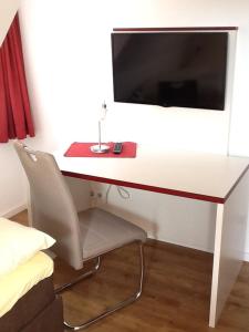 a desk with a chair and a television on a wall at Hotel Adler in Babenhausen