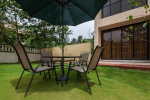 a table and chairs with an umbrella in a yard at StayVista's Greenwoods Villa 1 - City-Center Villa with Private Pool, Terrace, Lift & Carrom Board in Lonavala