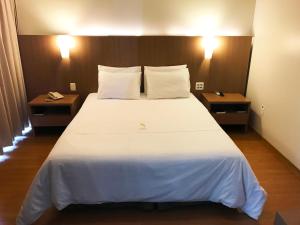 Sete Lagoas Residence Hotel في سيت لاغواس: غرفة نوم بسرير ابيض كبير مع طاولتين