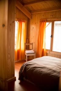 Schlafzimmer mit orangefarbenen Vorhängen, einem Bett und einem Stuhl in der Unterkunft El Refugio Casa de Montaña in San Martín de los Andes