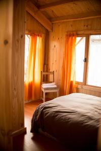 a bedroom with orange curtains and a bed and a chair at El Refugio Casa de Montaña in San Martín de los Andes