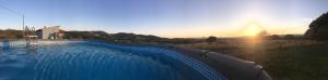 a large blue swimming pool in a field with the sunset at Agriturismo Sa Domo de s'Olia in Ozieri