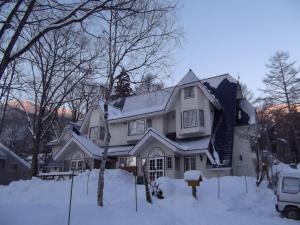 una casa blanca con nieve en el suelo en Pension Bonnard, en Hakuba