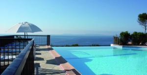 ein großer Pool mit Sonnenschirm und das Meer in der Unterkunft Mazet « Domaine de la pinède » in Le Lavandou
