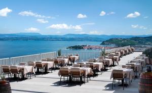 eine Reihe von Tischen und Stühlen auf einem Balkon neben dem Wasser in der Unterkunft Belvedere Resort Hotels in Izola