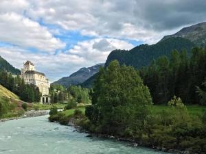 une rivière avec un bâtiment sur le flanc d'une montagne dans l'établissement Schloss Hotel & Spa Pontresina, à Pontresina