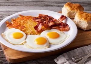 a plate of eggs and bacon on a wooden table at Splav "Slap" - Bungalovi in Danilovgrad