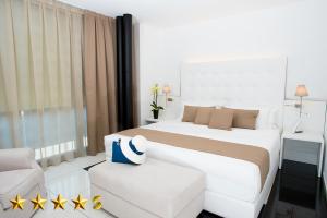 a white bedroom with a large bed and a chair at Hotel Rossini in Lignano Sabbiadoro