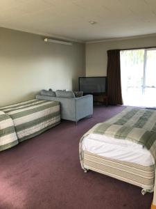 a bedroom with two beds and a couch and a television at Lilybrook Motel in Rangiora