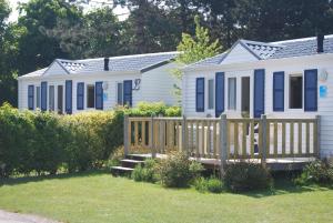 a white house with blue shutters and a wooden fence at Camping Le Walric in Saint-Valéry-sur-Somme