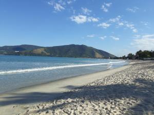 a sandy beach with the ocean and mountains in the background at Casa Condominio 250M Praia Maranduba Wifi Churrasqueira in Ubatuba