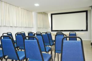 uma sala de aula com cadeiras azuis e uma tela de projeção em Hotel Vivendas Centro em Erechim