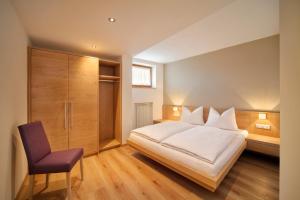 1 dormitorio con cama blanca y silla morada en Sonnenhof, en Rifiano