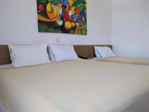 Simas Praia Hotel في أراكاجو: غرفة نوم بسرير ابيض مع لوحة على الحائط