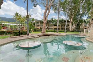 a swimming pool with trees and a building in the background at Amphora Laleuca Apartments Palm Cove in Palm Cove