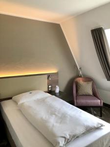 ein Schlafzimmer mit einem weißen Bett und einem Stuhl in der Unterkunft Hotel Am Park in Leinfelden-Echterdingen