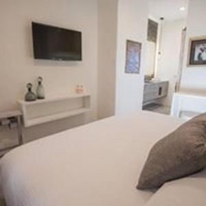 biała sypialnia z łóżkiem z telewizorem na ścianie w obiekcie Hotel de Piedra w mieście Bernal