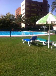 2 ligstoelen en een parasol naast een zwembad bij Apartamentos La Roca Rentals in Torremolinos