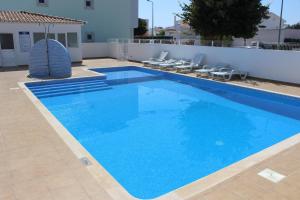 a large blue swimming pool with chairs and a building at Alta da Ria House in Cabanas de Tavira