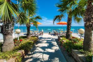 uma passarela com palmeiras e cadeiras e a praia em Hotel Olimpic em Martinsicuro