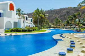 a resort swimming pool with blue water and palm trees at 2062 - Lu Iba Condo 1 in Santa Cruz Huatulco