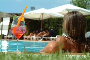 a woman laying next to a swimming pool with a drink at Andrea Doria Hotel in Marina di Ragusa