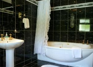 Baño de azulejos negros con lavabo y bañera en Hanora's Cottage Guesthouse and Restaurant, en Ballymacarbry