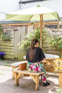 une femme assise sur une table de pique-nique sous un parapluie dans l'établissement Route 2 Apartments, à Topsham