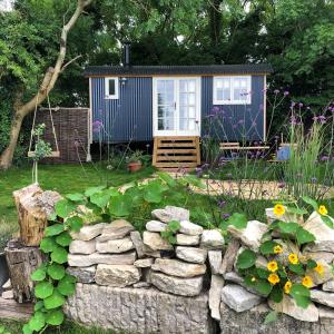 a tiny house in a garden with a stone wall at Purbeck Shepherd Huts in Worth Matravers