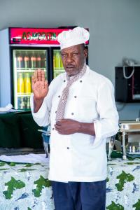 Un uomo con un cappello da chef che alza la mano di Asmorein Hotel a Babati