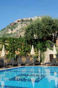 a swimming pool with chairs and umbrellas next to a mountain at Villa Angela in Taormina