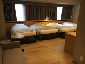 ein Hotelzimmer mit 3 Betten und einem Tisch in der Unterkunft Hotel Monte Hermana Fukuoka in Fukuoka