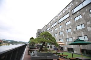 a building with tables and umbrellas next to a river at Hotel Dongbang in Jinju
