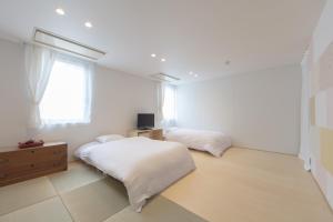 a white bedroom with two beds and a window at Crasco TABI-NE in Kanazawa