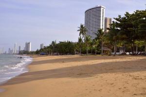 een strand met palmbomen en een hoog gebouw bij Sunshine Beach Condotel in Na Jomtien