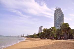 a beach with palm trees and a tall building at Sunshine Beach Condotel in Na Jomtien
