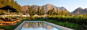a pool with chairs and an umbrella and mountains at La Clé Village in Franschhoek