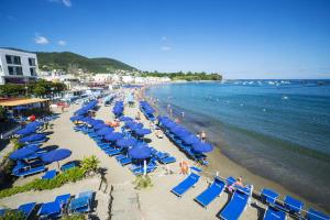 a beach with blue chairs and people in the water at Casthotels Bristol Terme in Ischia