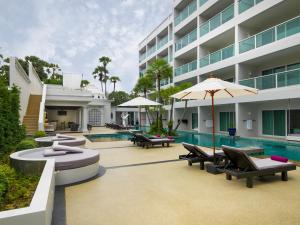 a pool with chairs and umbrellas next to a building at Chanalai Romantica Resort - Adults Only, Kata Beach in Kata Beach