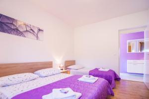 2 Betten in einem Zimmer mit lila Bettwäsche und Handtüchern in der Unterkunft Apartmani Perkovic in Gustirna