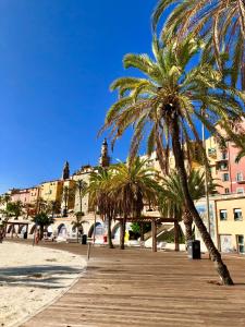 a boardwalk on a beach with palm trees and buildings at Les Sablettes in Menton