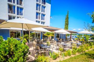 eine Terrasse mit Tischen und Sonnenschirmen vor einem Gebäude in der Unterkunft Hôtel Côté Sud Léman in Thonon-les-Bains