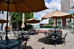 eine Außenterrasse mit Tischen, Stühlen und Sonnenschirmen in der Unterkunft Country Hotel & Suites in Guadalajara