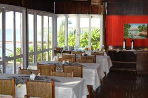 a restaurant with white tables and chairs and windows at Pousada Corumbau in Corumbau