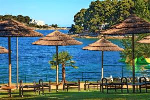 a group of tables and straw umbrellas next to the water at Apartment Marino in Poreč